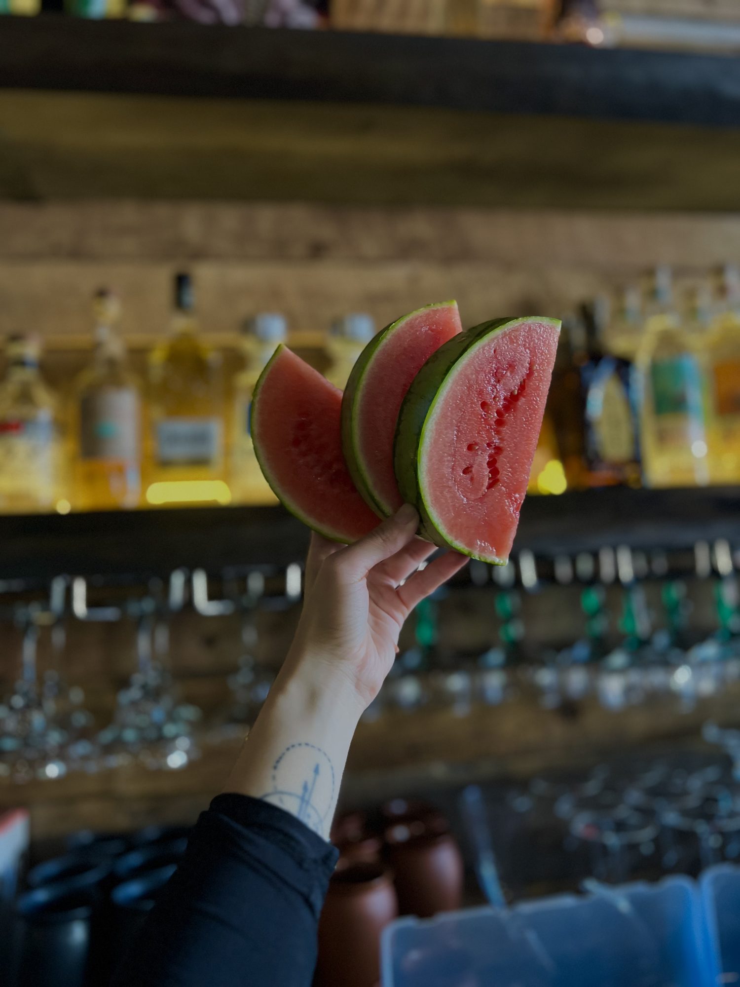 A bartender holding fresh watermelon in front of the stocked back bar