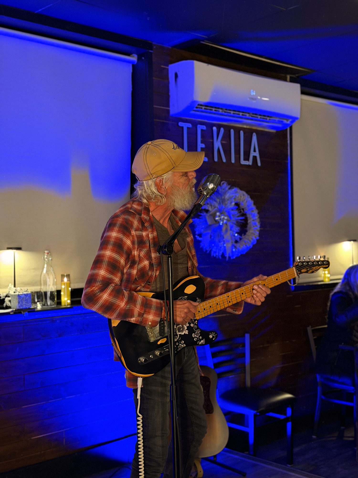 A guitarist performing under a blue Tekila sign