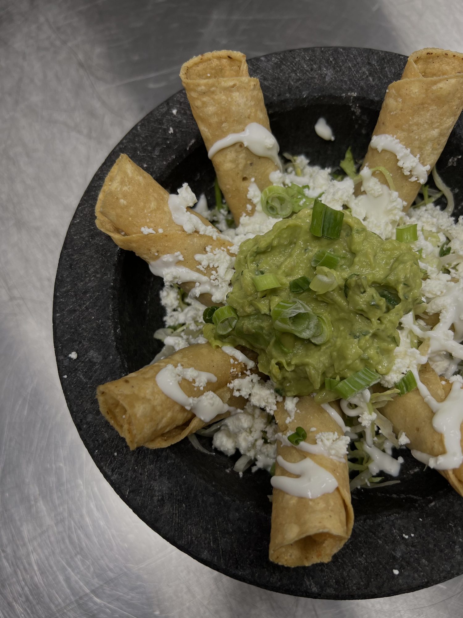 Tacos dorados arranged around a mound of fresh guacamole